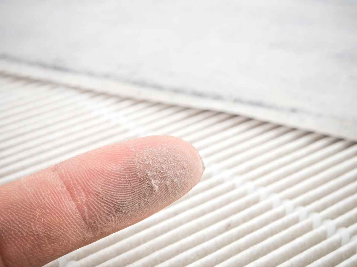 dust on finger with dirty HVAC filter in the background