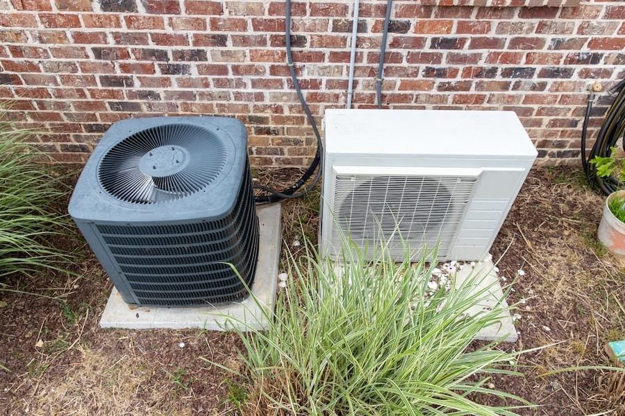 Outdoor air conditioning unit and heat pump on the side of a brick house