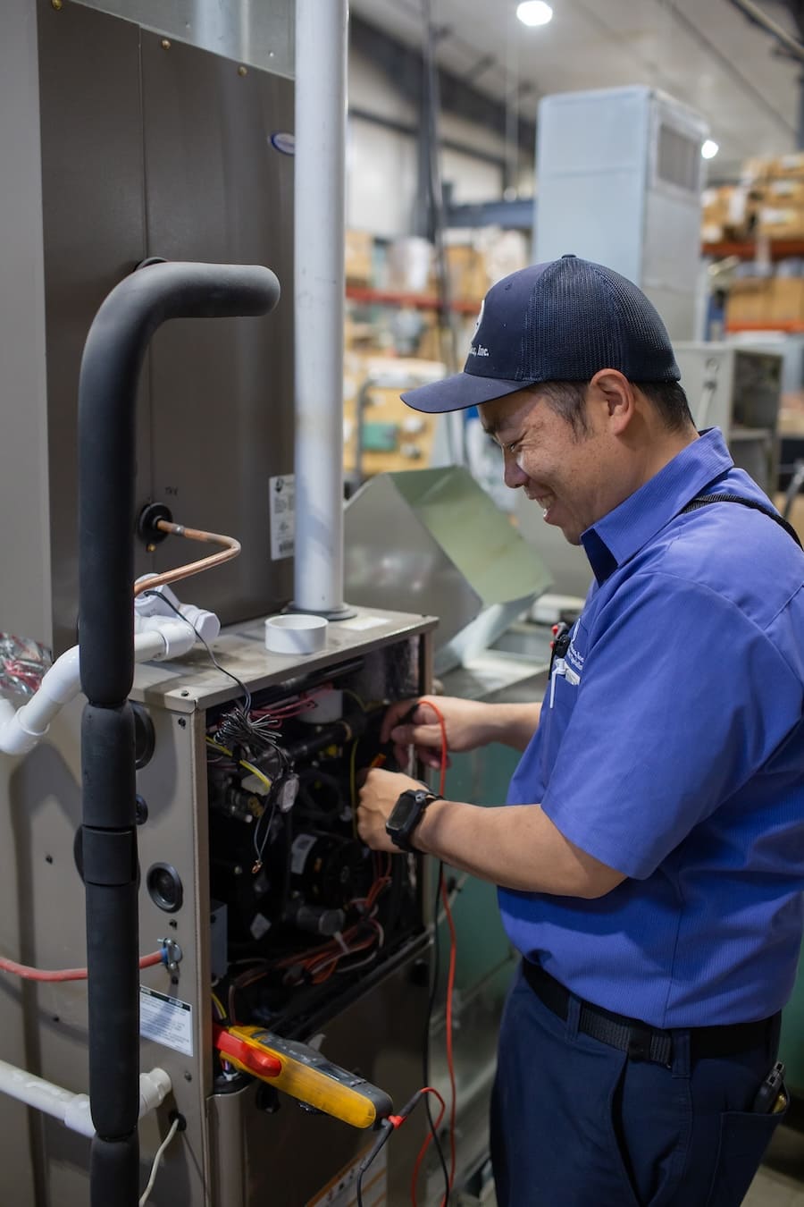 Technician in blue uniform repairs an open industrial machine with wires and tools inside a workshop.